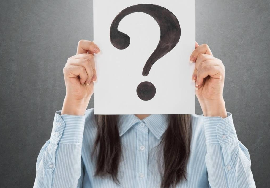 A women holding a piece of paper with a question mark on it that's covering her face.