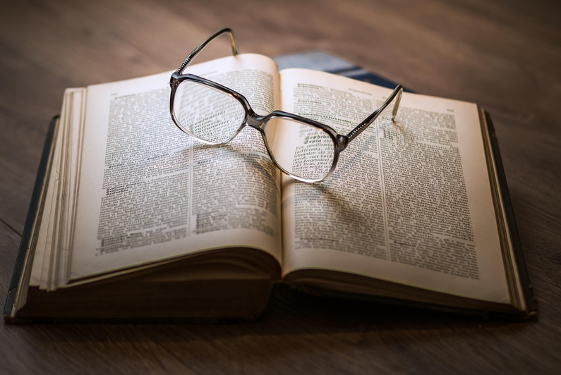 A picture of a open book with a pair of glasses on them.